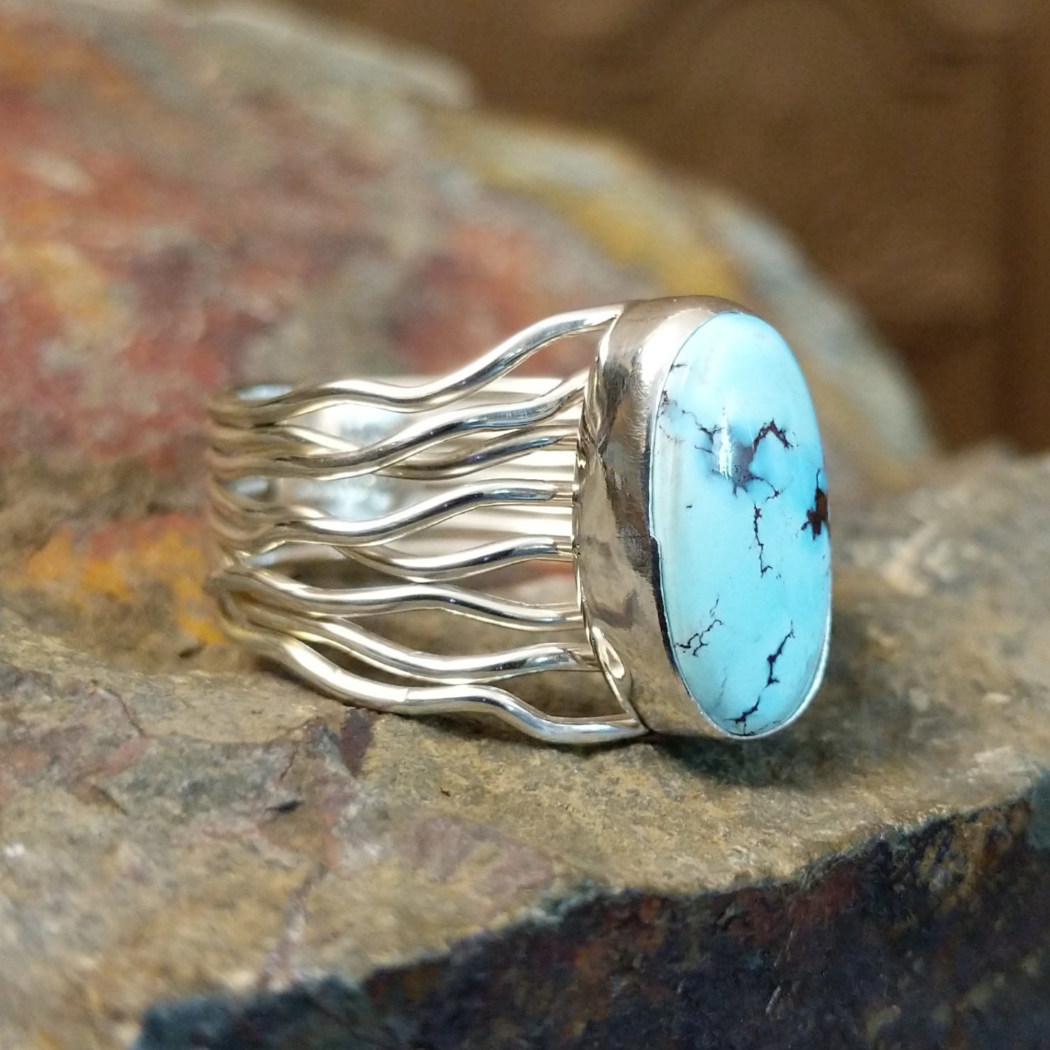 Silver ring with a smooth bezel holding an oval turquoise stone, its twisted silver band.