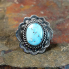 Silver ring with a large oval turquoise stone in a smooth bezel. Twisted rope and scalloped edge surround the stone with matrix veining.