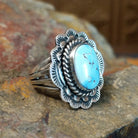 Silver ring with a smooth bezel holding a large oval turquoise stone. Twisted rope and scalloped edge visible with matrix veining.