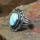 Silver ring with a smooth bezel holding a large oval turquoise stone. Twisted rope and scalloped edge visible with matrix veining.