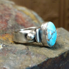 Silver ring with a smooth bezel holding an oval turquoise stone and raised silver detailing on the band.