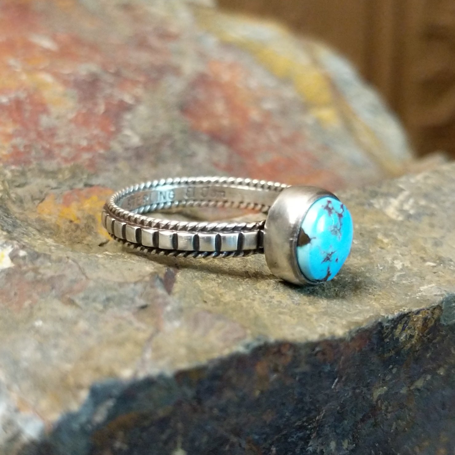 Silver ring with a smooth bezel holding a round turquoise stone, its twisted, ribbed band adding texture.