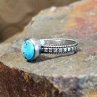 Silver ring with a smooth bezel holding a round turquoise stone, its twisted, ribbed band adding texture.