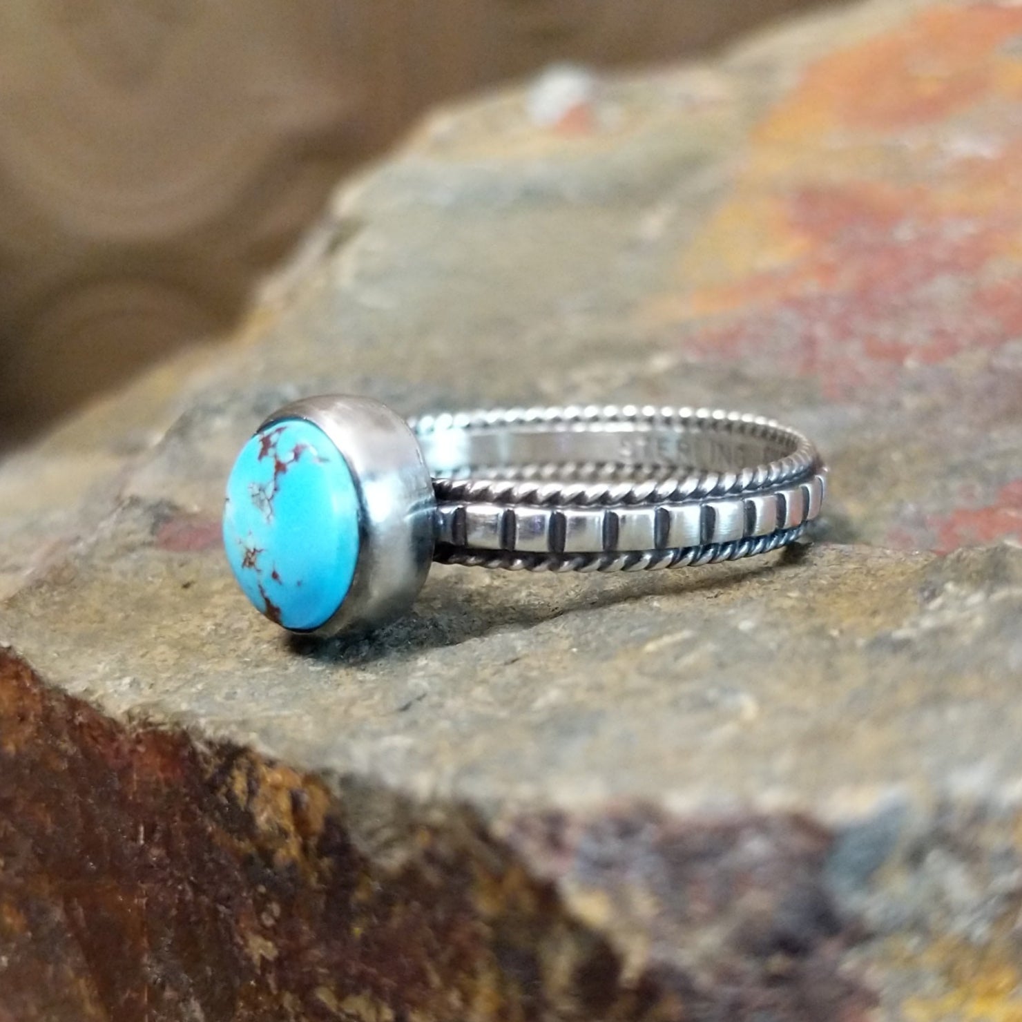 Silver ring with a smooth bezel holding a round turquoise stone, its twisted, ribbed band adding texture.