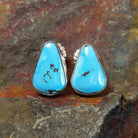 The golden hills turquoise triangular earrings by Diane Wylie feature vibrant turquoise stones with a brown matrix, set in a simple silver bezel. Their triangular shape captures Southwest Native American elegance.