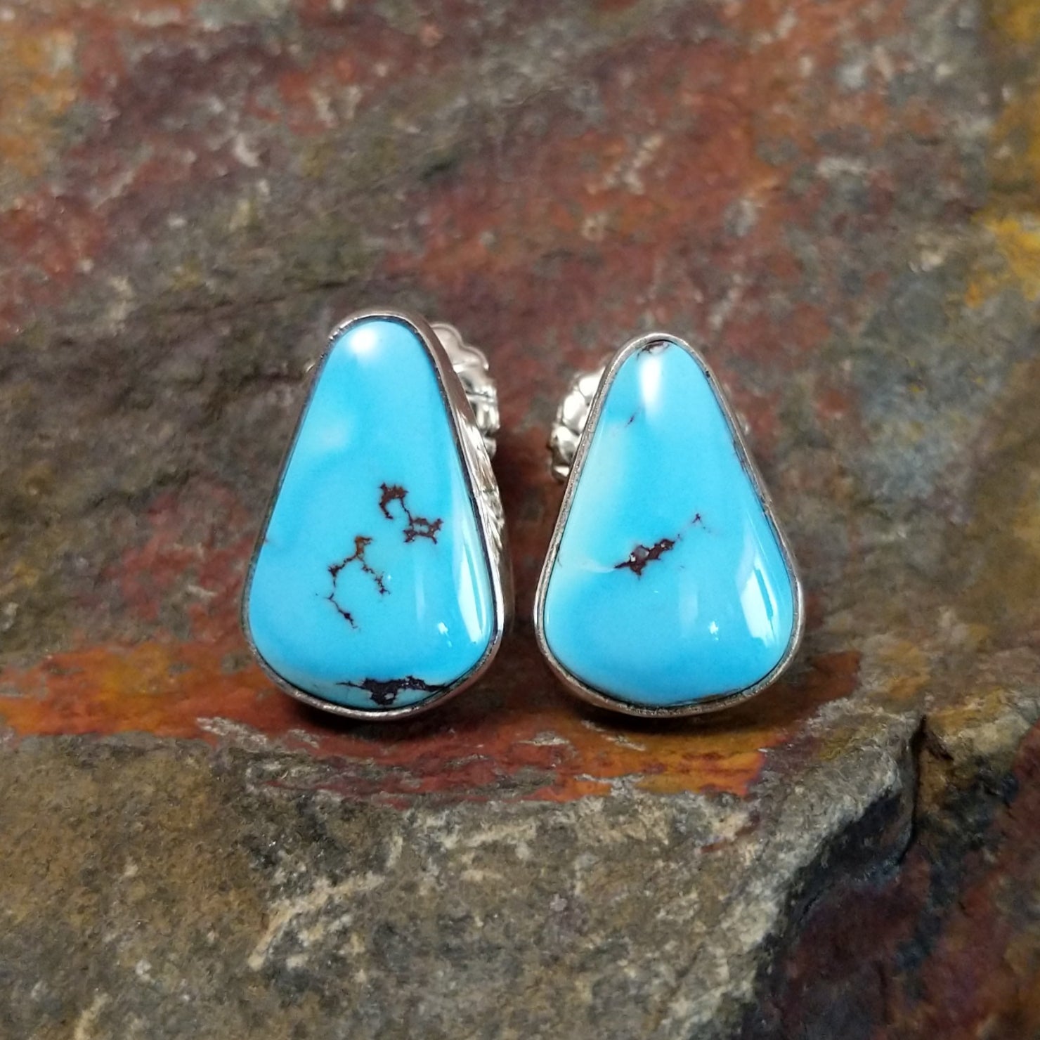 The golden hills turquoise triangular earrings by Diane Wylie feature vibrant turquoise stones with a brown matrix, set in a simple silver bezel. Their triangular shape captures Southwest Native American elegance.