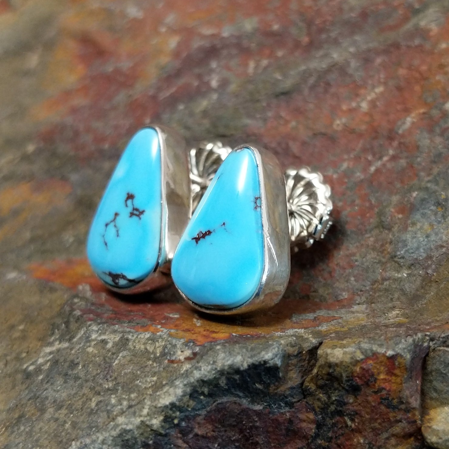 A side view of the golden hills turquoise triangular earrings by Diane Wylie shows the turquoise stone’s smooth edge in a simple bezel. The silver post shines against the stone’s vivid blue.