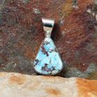 The front view of the pendant showcases a triangular golden hills turquoise stone with a brown matrix, set in a simple silver bezel. A polished silver bail adds a sleek touch.