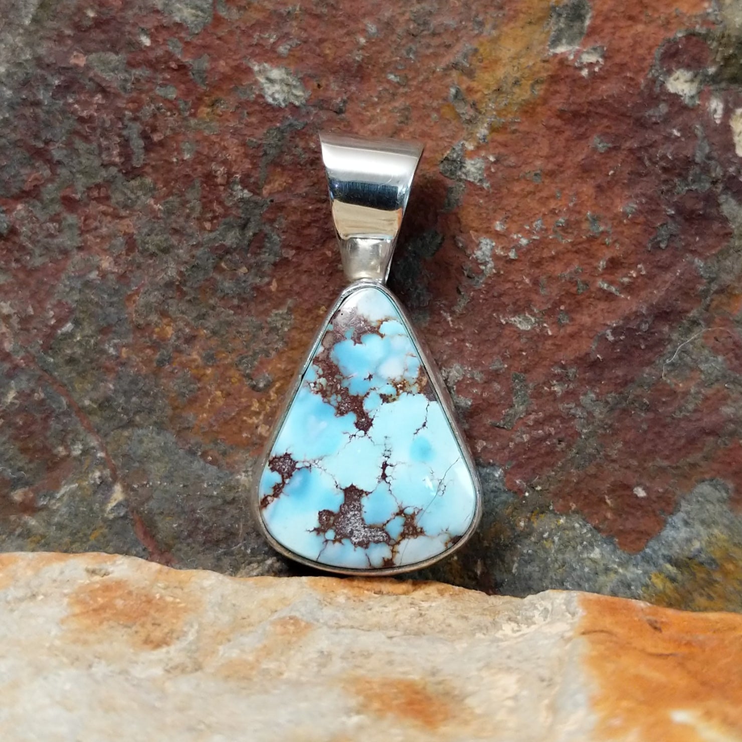 The front view of the pendant showcases a triangular golden hills turquoise stone with a brown matrix, set in a simple silver bezel. A polished silver bail adds a sleek touch.