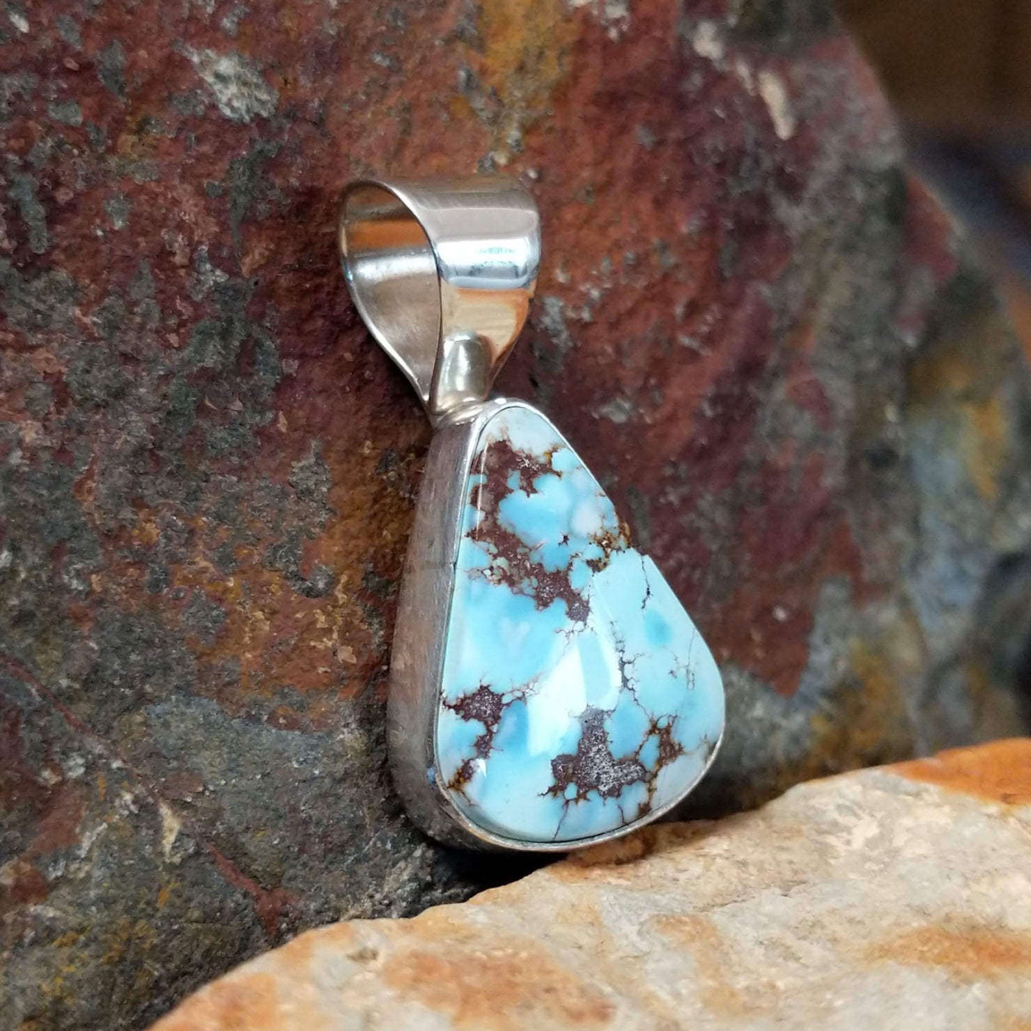 A side view reveals the triangular turquoise stone’s brown matrix in a simple silver bezel, with the silver bail shining. 