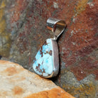 A side view reveals the triangular turquoise stone’s brown matrix in a simple silver bezel, with the silver bail shining. 