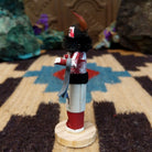 Mini grandmother kachina by Rosalind Grey with red body, black fur collar, feathered headpiece, and white geometric-patterned garment.