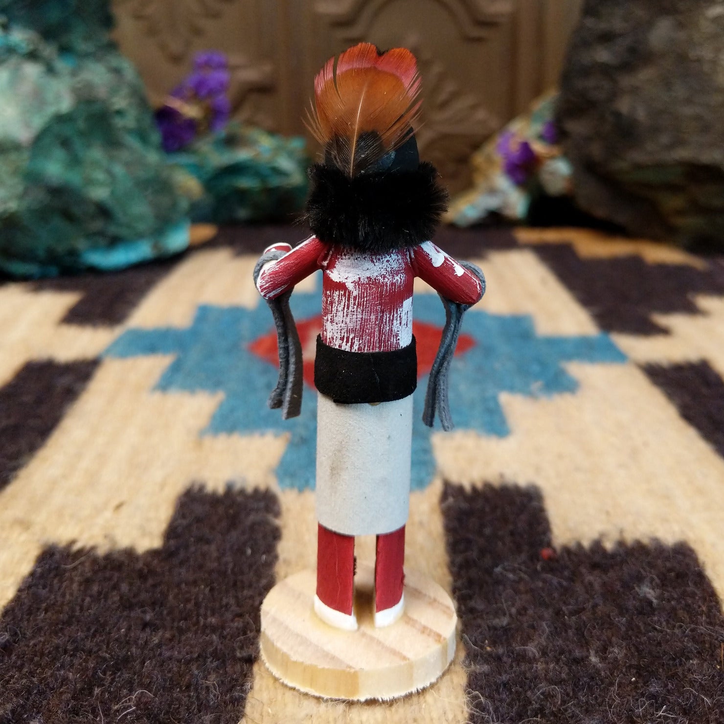 Mini grandmother kachina by Rosalind Grey with red body, black fur collar, feathered headpiece, and white geometric-patterned garment.