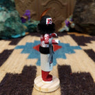 Mini grandmother kachina by Rosalind Grey with red body, black fur collar, feathered headpiece, and white geometric-patterned garment.