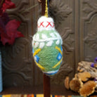 This delightful Green Bulb Wool Ornament by Ganz features a soft green wool body decorated with blue and yellow floral accents, white leaf patterns, a fluffy white top with red stitching, and a gold hanging cord.