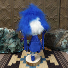 Navajo-made Hemis kachina doll by M. C. with blue feathered headdress, raised leg, and multicolored painted mask.