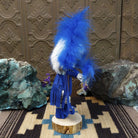 Navajo-made Hemis kachina doll by M. C. with blue feathered headdress, raised leg, and multicolored painted mask.