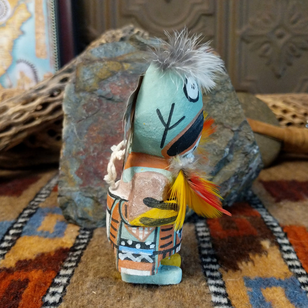 Wood carved into a frog kachina doll, painted with vibrant colors and feathers adorning its' body.