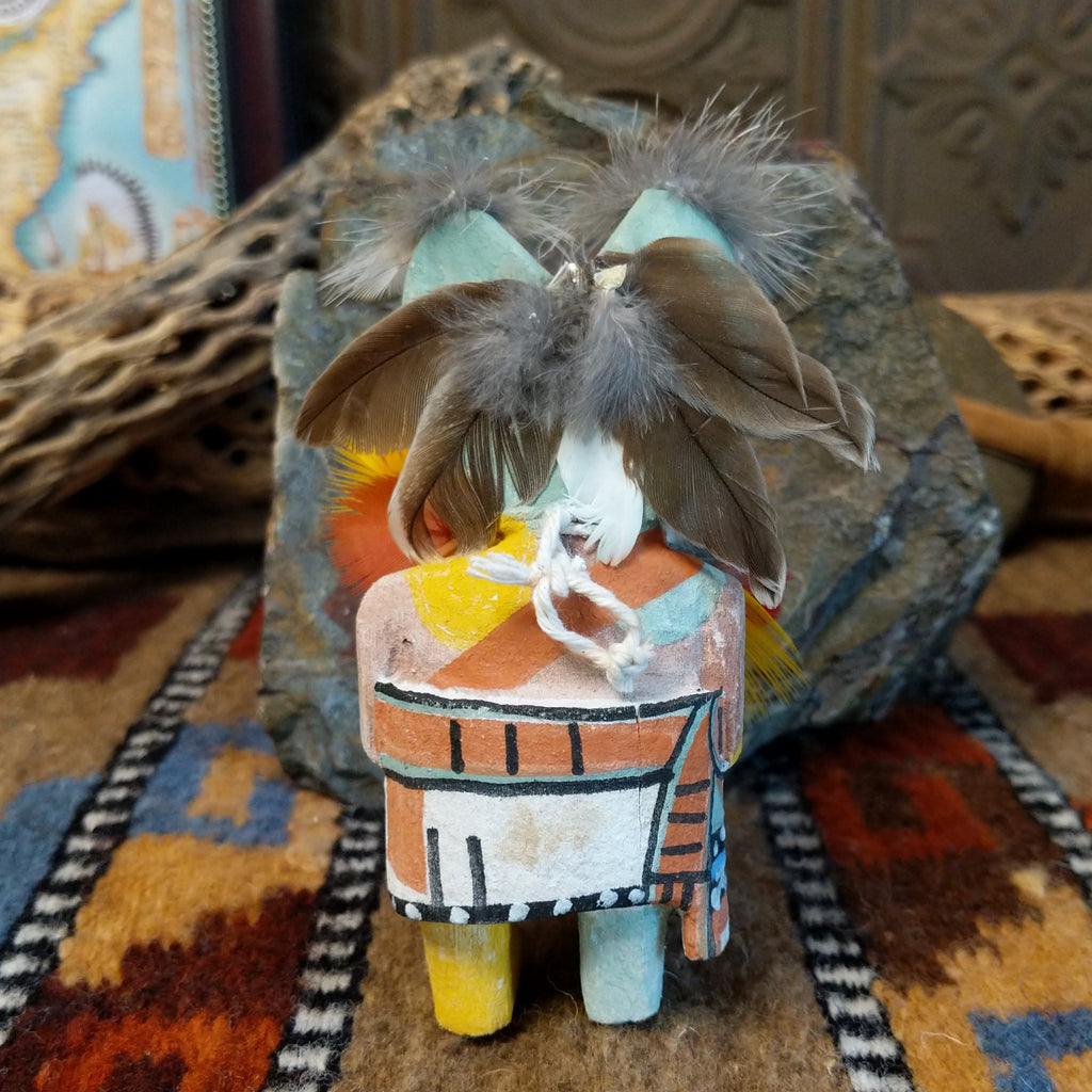 Wood carved into a frog kachina doll, painted with vibrant colors and feathers adorning its' body.