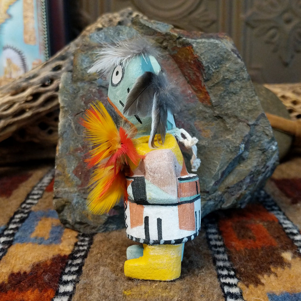 Wood carved into a frog kachina doll, painted with vibrant colors and feathers adorning its' body.