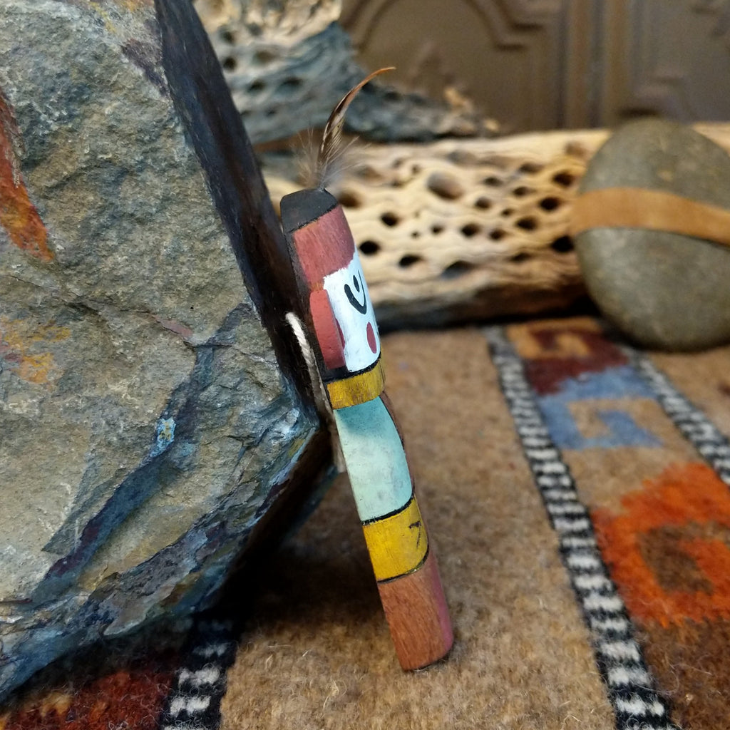 Wood carved into a grandmother kachina and painted with vibrant cololors with a singular feather on the top of its' head.