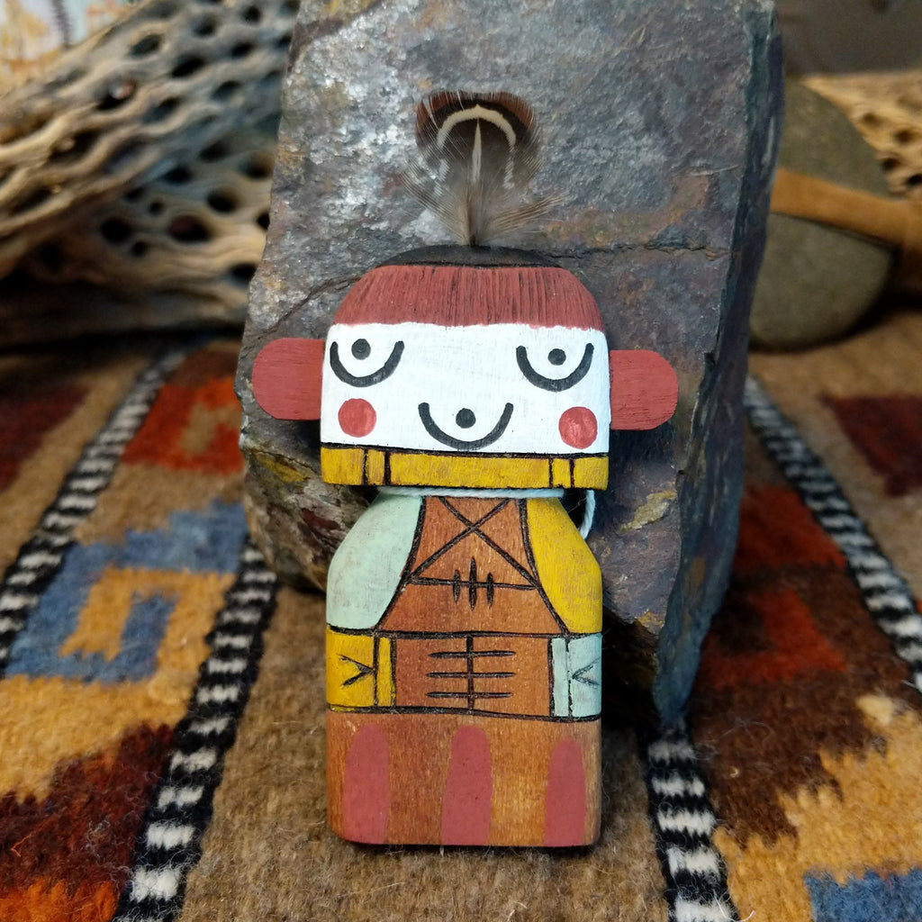 Wood carved into a grandmother kachina and painted with vibrant cololors with a singular feather on the top of its' head.