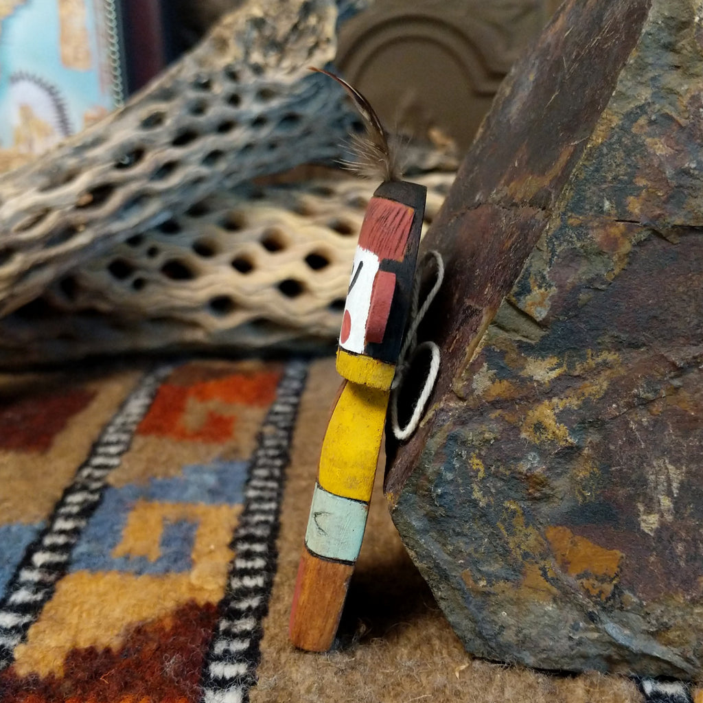 Wood carved into a grandmother kachina and painted with vibrant cololors with a singular feather on the top of its' head.