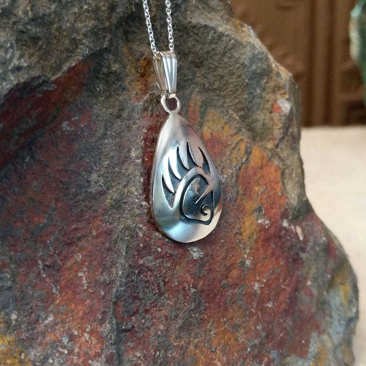Hopi silver bear paw pendant by Loren Sakeva featuring a teardrop shape with polished silver and darkened recessed overlay-style detailing; side view.