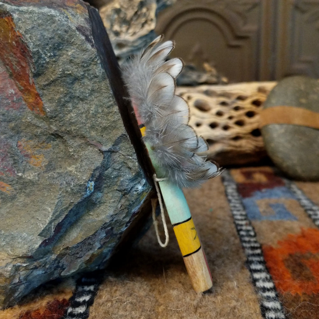 Wood carved into a sunface, painted with vibrant colors and features feathers.