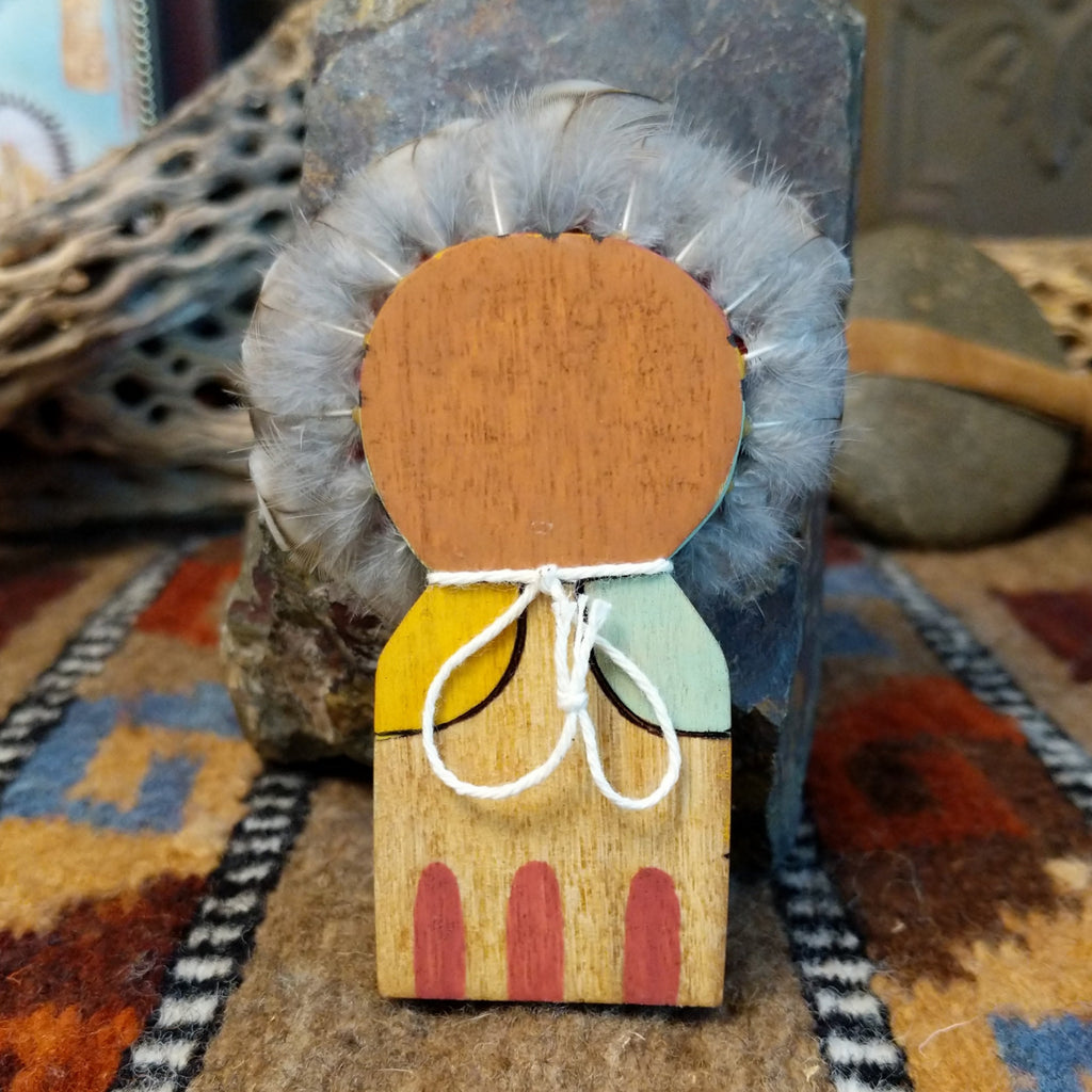 Wood carved into a sunface, painted with vibrant colors and features feathers.