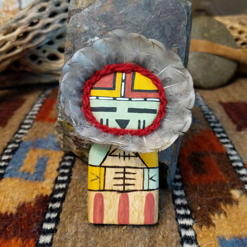 Wood carved into a sunface kachina, painted with vibrant colors and features feathers.