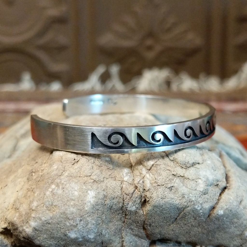 Sterling silver cuff with wave motifs stamped on the surface.