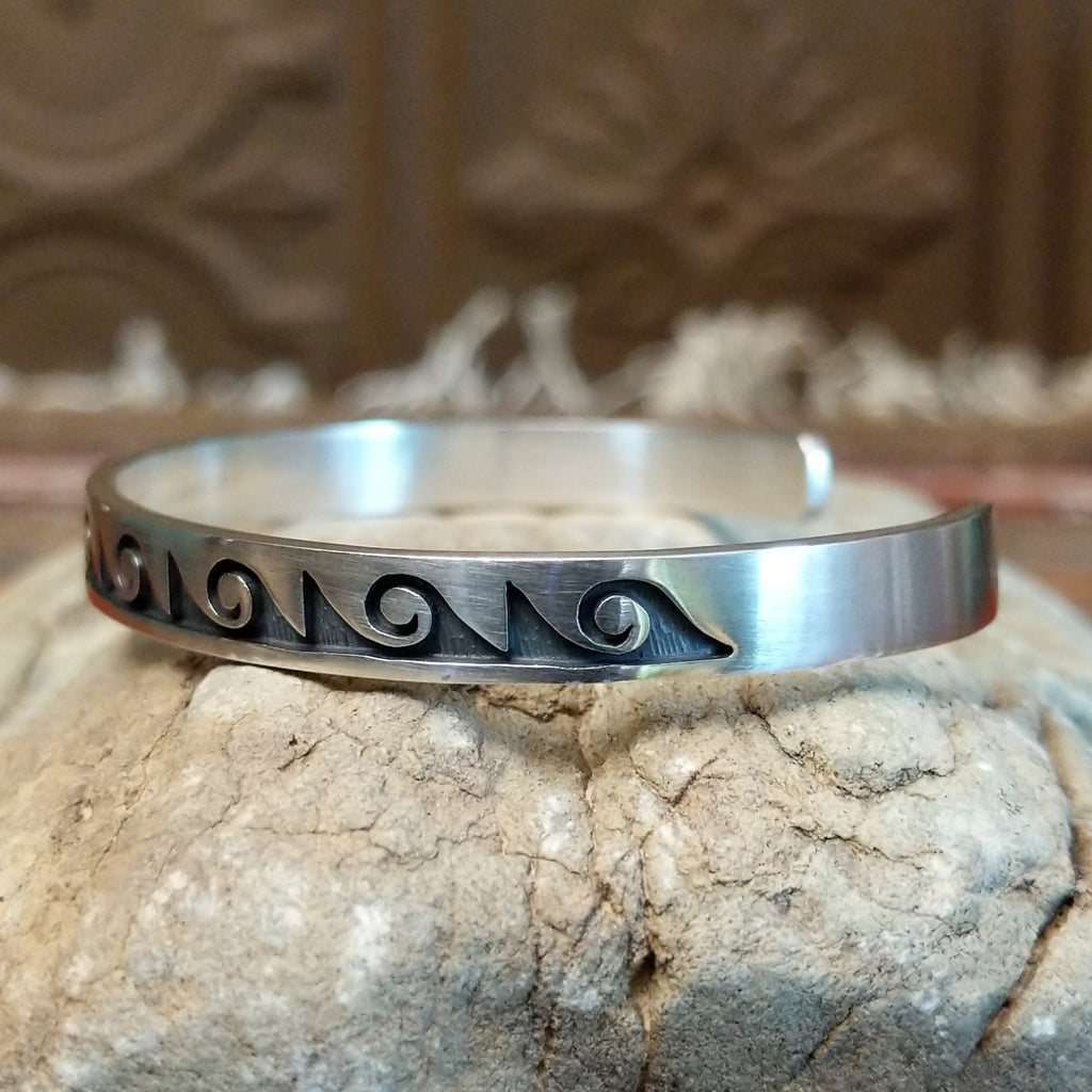 Sterling silver cuff with wave motifs stamped on the surface.