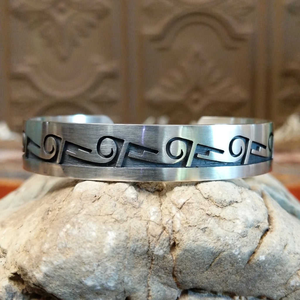 Sterling silver cuff with whirlwind and rain cloud motifs on the surface.