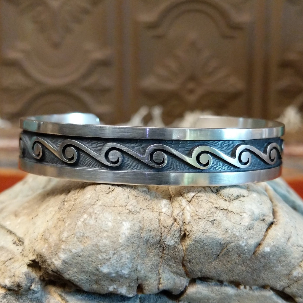 Sterling silver cuff with whirlwind motifs stamped on the surface.
