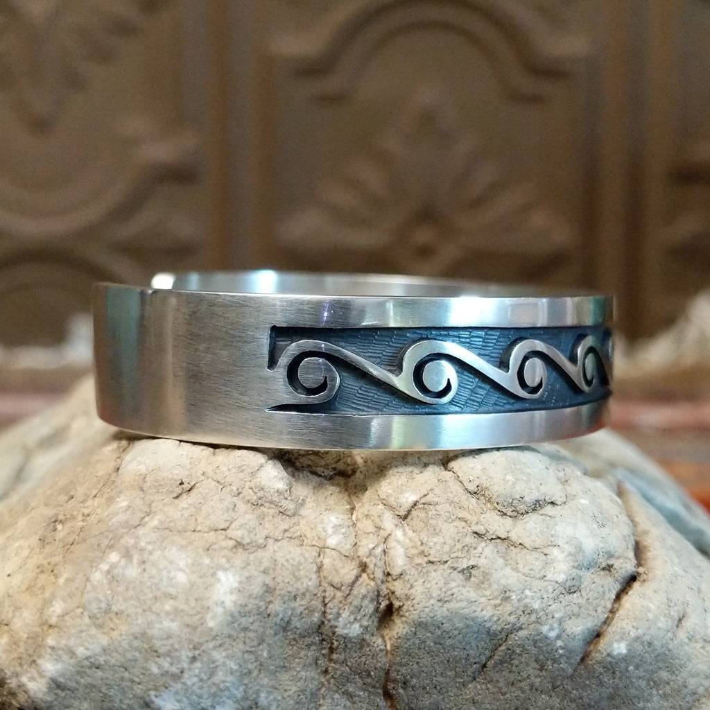 Sterling silver cuff with whirlwind motifs stamped on the surface.
