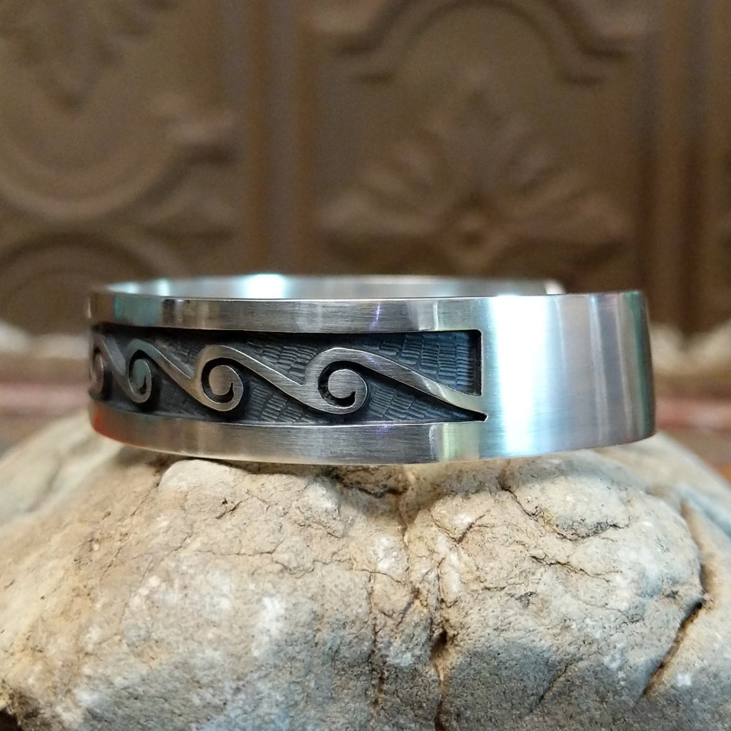 Sterling silver cuff with whirlwind motifs stamped on the surface.