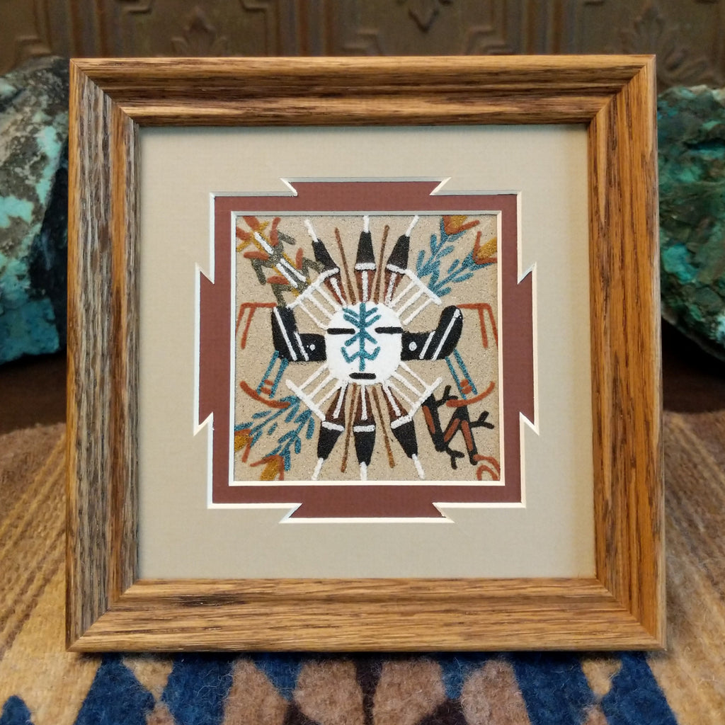 Sand painting of a horned figure in various colors with a wooden frame.