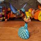 Polymer clay used to create a removable hummingbird and cactus, both painted vibrantly with floral motifs.
