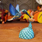 Polymer clay used to create a removable hummingbird and cactus, both painted vibrantly with floral motifs.