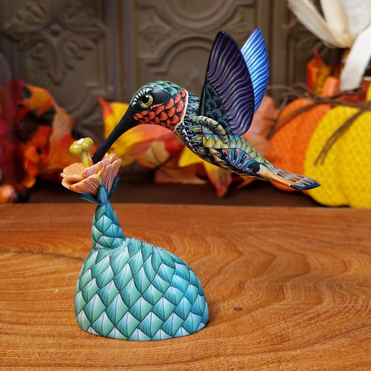 Polymer clay used to create a removable hummingbird and cactus, both painted vibrantly with floral motifs.