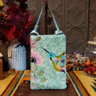 Hummingbird Club Bag by Bamboo Trading featuring a colorful turquoise blue hummingbird surrounded by pink flowers and green leaves on a shimmering mint green beaded background, with a coordinating light blue strap.