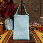 Hummingbird Club Bag by Bamboo Trading featuring a colorful turquoise blue hummingbird surrounded by pink flowers and green leaves on a shimmering mint green beaded background, with a coordinating light blue strap; back side view.