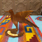 Handcrafted Crooks Design metal hummingbird tabletop sculpture with outstretched wings, detailed feather cutouts, a warm burnished finish, and a decorative base marked Tombstone, AZ; side view.