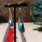 Kingman turquoise earrings by Everett & Mary Teller featuring elongated textured sterling silver drops with oval blue turquoise stones and French wire hooks; side view.