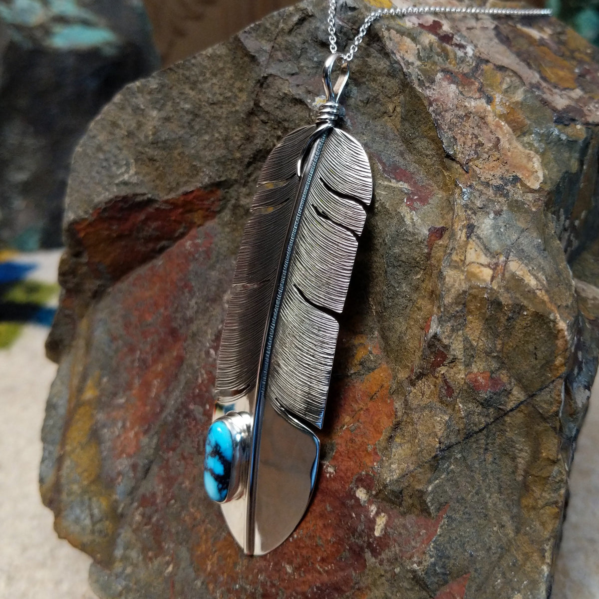 Kingman Turquoise feather pendant by Lena Platero featuring a detailed silver feather with etched texture, polished accents, and an oval turquoise stone with dark matrix; side view.