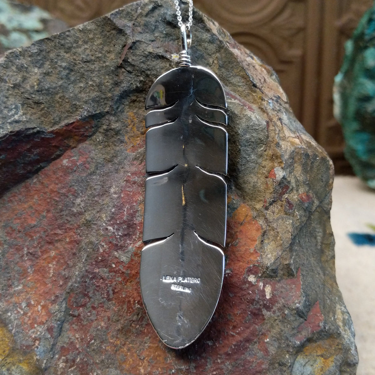 Kingman Turquoise feather pendant by Lena Platero featuring a detailed silver feather with etched texture, polished accents, and an oval turquoise stone with dark matrix; artisan and Sterling Silver stamp.