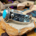 Handcrafted sterling silver Navajo cuff by Charlene & Robert Little featuring an oval Kingman turquoise cabochon with a twisted rope bezel, scalloped silver border, and hand-stamped concho accents; side view.