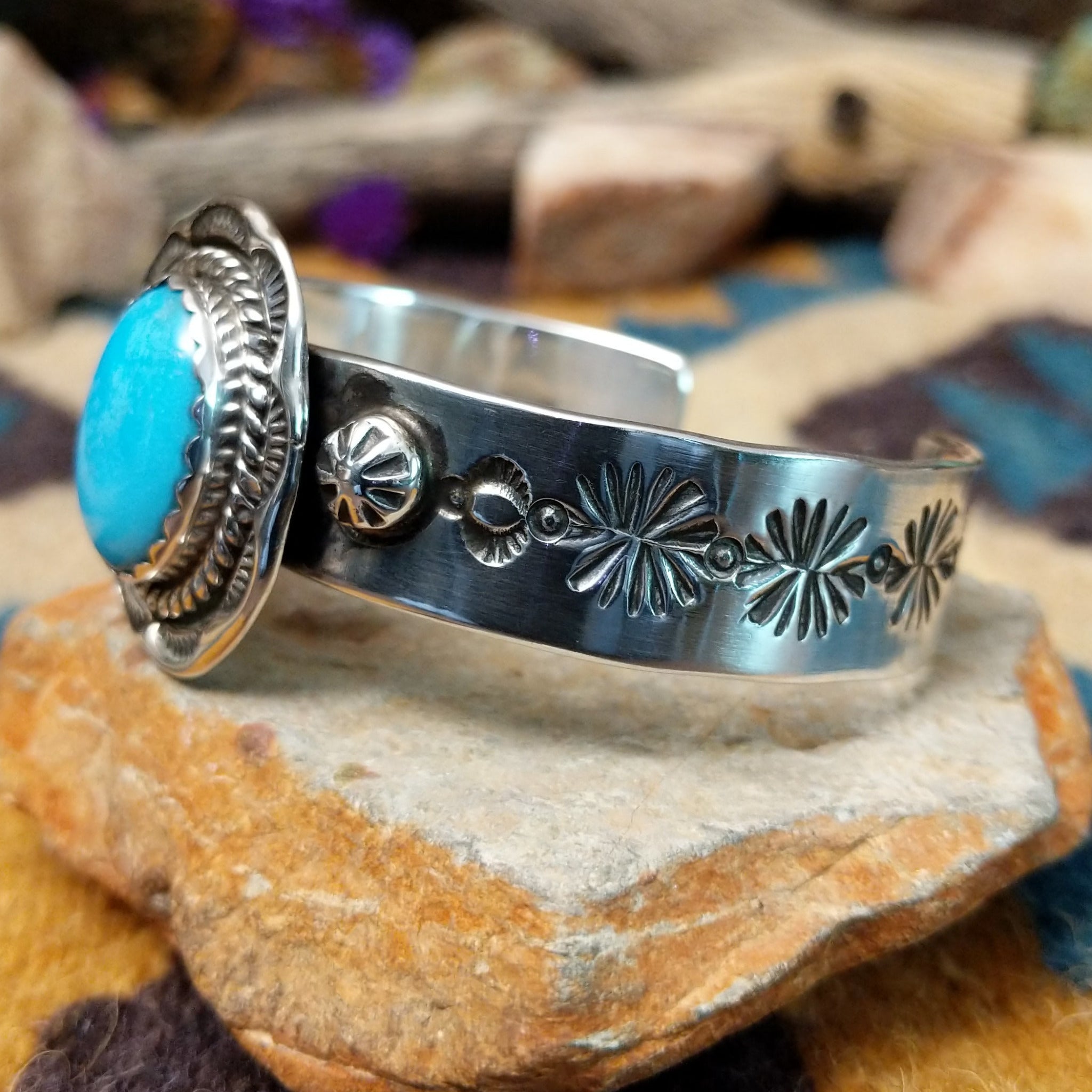 Handcrafted sterling silver Navajo cuff by Charlene & Robert Little featuring an oval Kingman turquoise cabochon with a twisted rope bezel, scalloped silver border, and hand-stamped concho accents; side view.