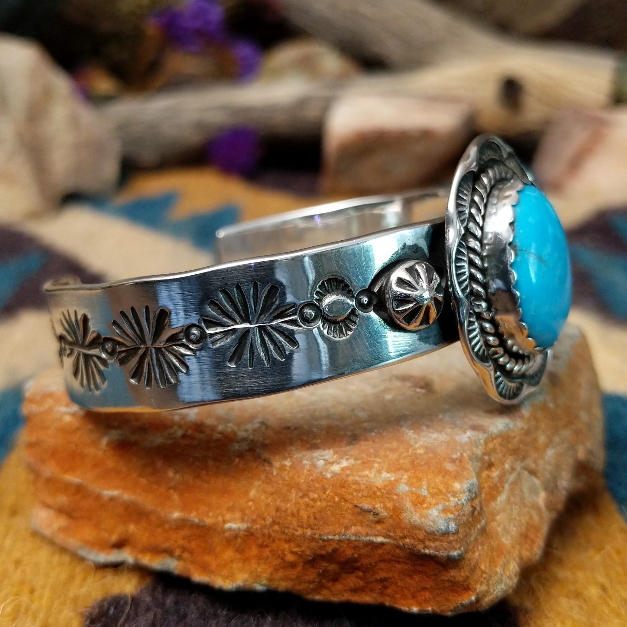Handcrafted sterling silver Navajo cuff by Charlene & Robert Little featuring an oval Kingman turquoise cabochon with a twisted rope bezel, scalloped silver border, and hand-stamped concho accents; side view.